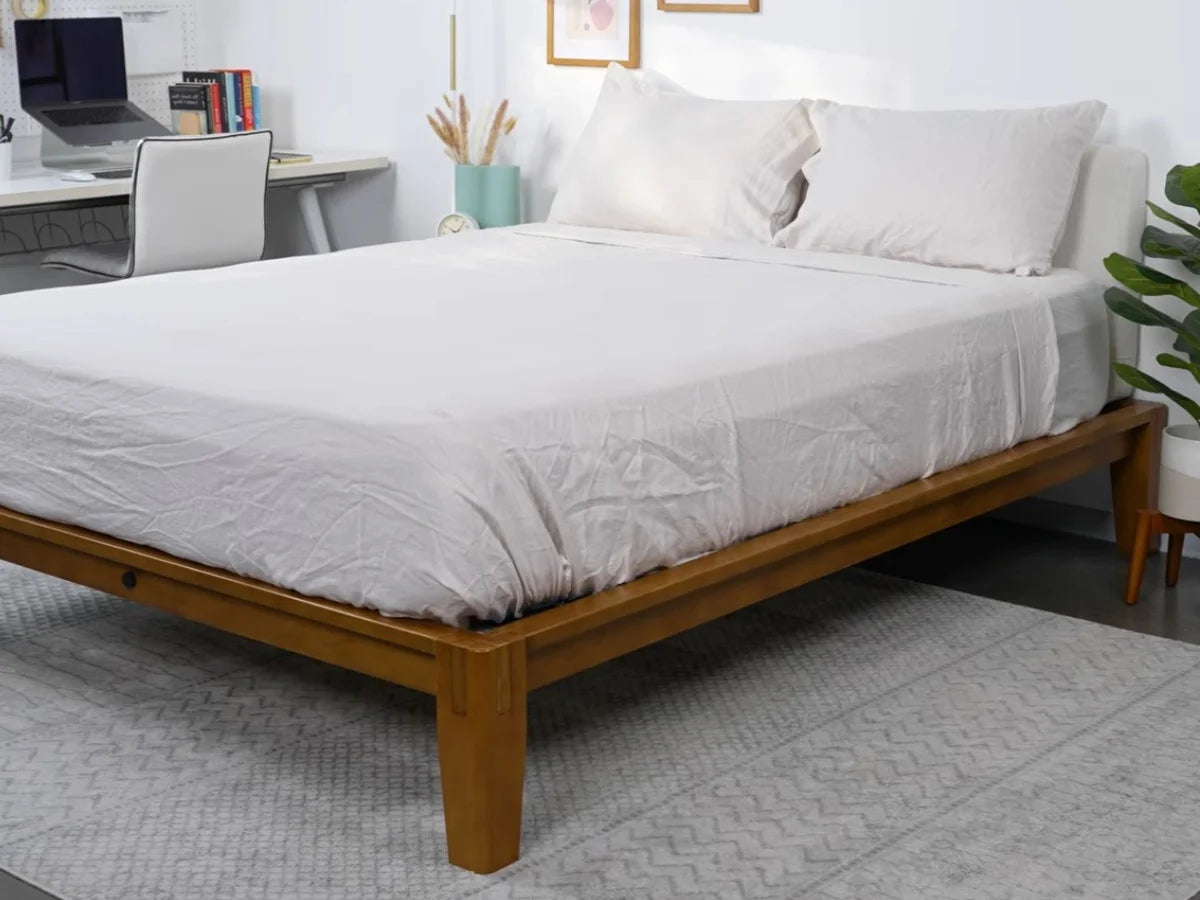 White bed sheets and pillowcases styled on a wooden bed in a bright modern bedroom with a home workspace.