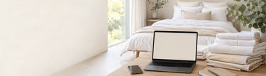Linen King Australia customer support workspace with folded bed linen and towels beside a laptop in a bright bedroom.