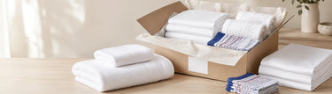 White bed sheets, bath towels and checked kitchen towels packed in a box for Linen King Australia shipping.